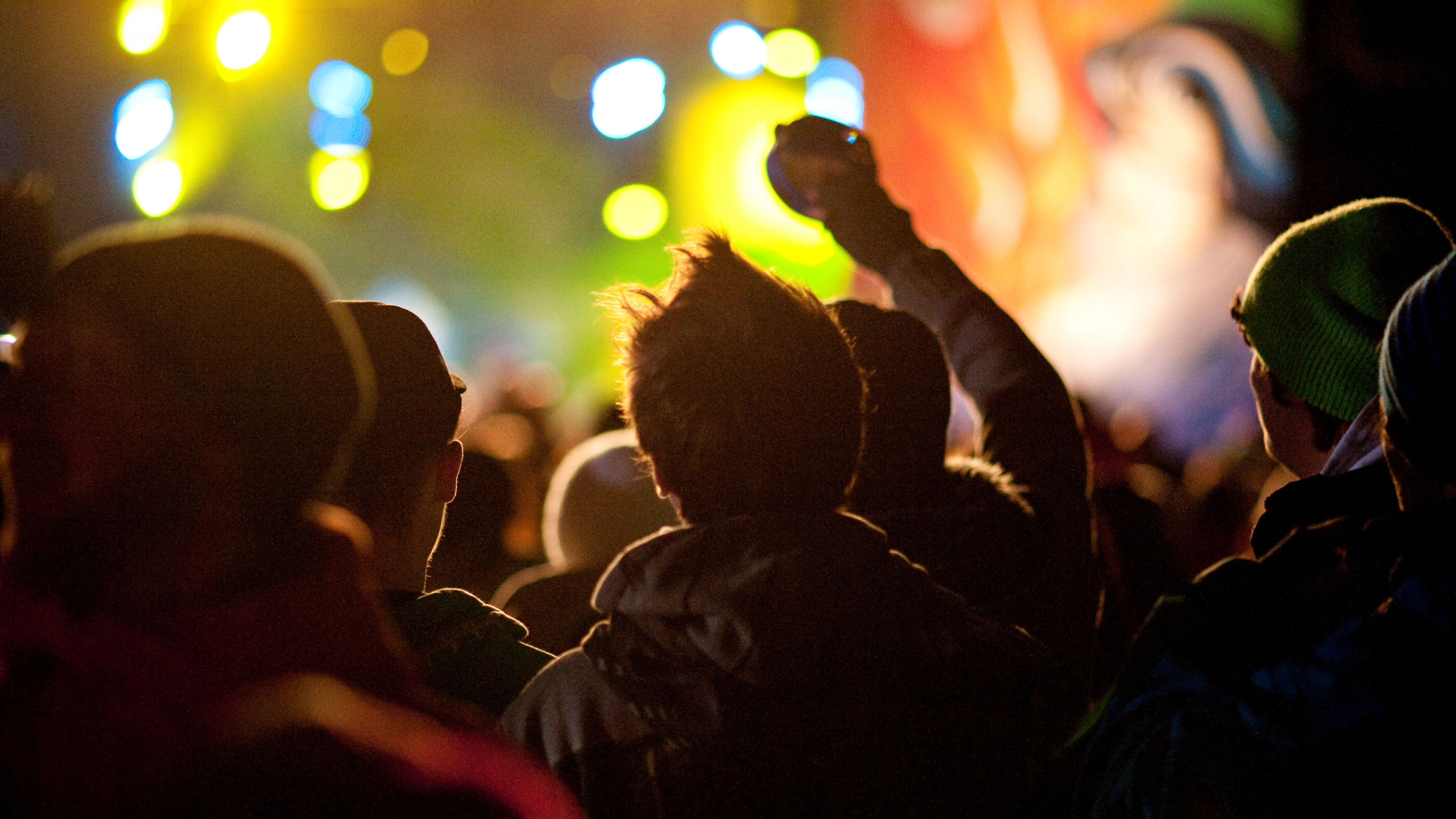 A crowd at a live event facing a stage lit with colourful lights.