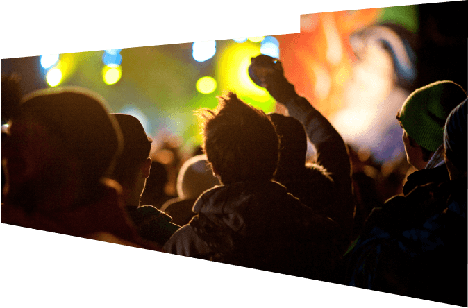 A crowd at a live event facing a stage lit with colourful lights.