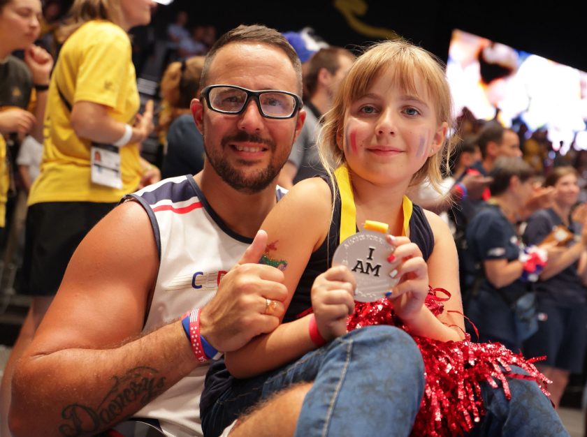 A daughter sitting in her fathers lap and holding an Invictus Games medal – clicking this link will open a larger version of it in the browser window.