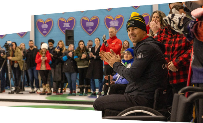 A man in a wheelchair glances at the camera among a crowd of applauding spectators.