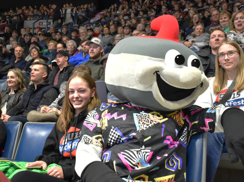 Curling Canada's mascot, Slider, sits with a young smiling fan in the stands at the 2024 Montana's Brier – clicking this link will open a larger version of it in the browser window.
