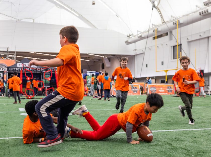 A group of children in BC Lions shirts falling over each other as they play with a football – clicking this link will open a larger version of it in the browser window.